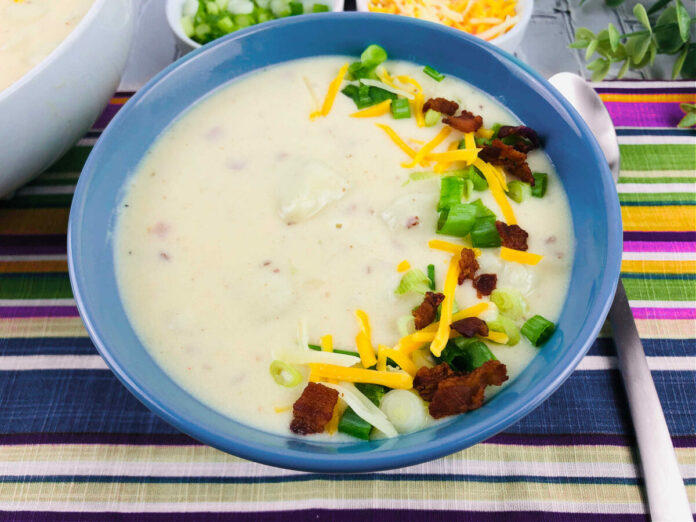 side view of a bowl of loaded baked potato soup garnished with bacon, cheese, and green onions