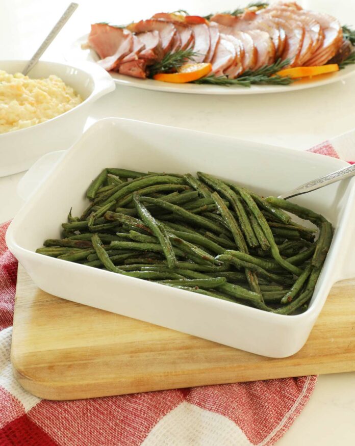 Baked Green Beans in a white serving dish on a wooden cutting board.