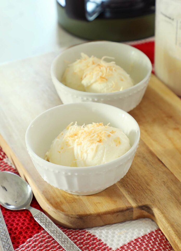 Two bowls of pina colada ice cream on a wooden cutting board topped with toasted coconut.